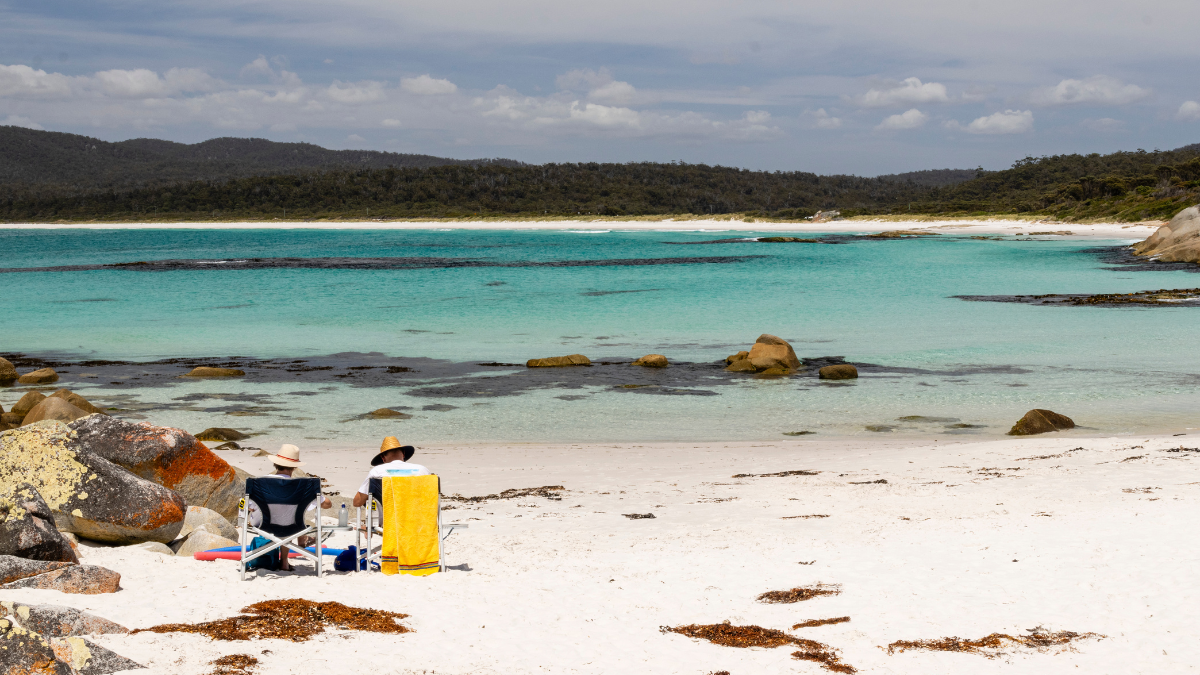 Beach by waterside with 2 people sitting on chairs